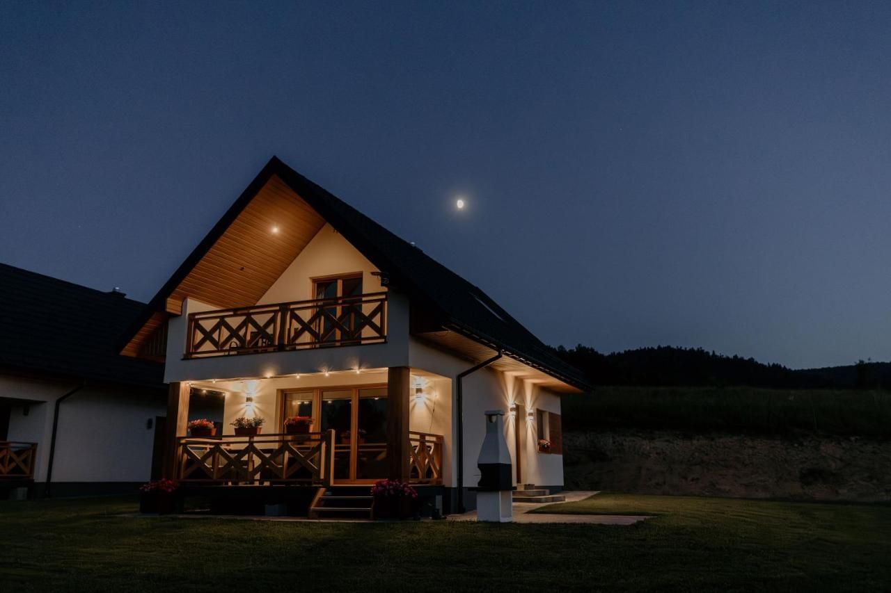 Domek wieczorem, z oświetlonym tarasem i balkonem pod ciemnym niebem